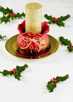 Gold candle in Christmas pot with holly leaves