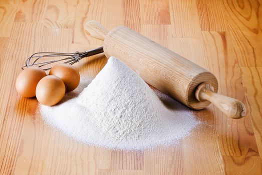 Flour with eggs, rolling pin and beater on the wooden table