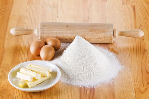 Flour with eggs, rolling pin and butter on the wooden table