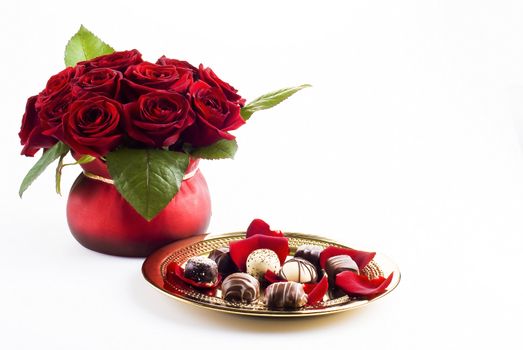 Beautiful roses in pot with gold plate of chocolates