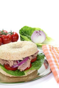 Bagel with tuna, tomatoes, onions, and lettuce on white background