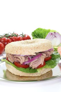 Bagel with tuna, tomatoes, onions, and lettuce on white background