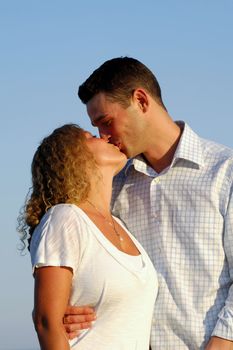 A sweet young couple is kissing in the sun.