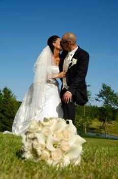 A wedding couple is kissing. The bouquet is in blur