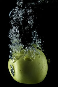 A green apple splashing on a water surface with a black background.