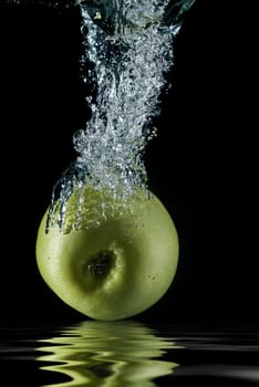 A green apple splashing on a water surface with a black background.