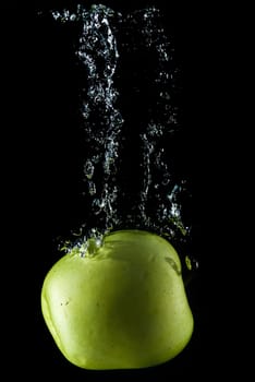 A green apple splashing on a water surface with a black background.