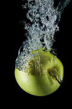 A green apple splashing on a water surface with a black background.