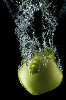 A green apple splashing on a water surface with a black background.