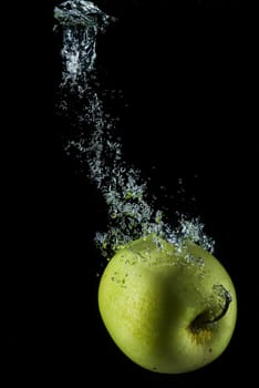 A green apple splashing on a water surface with a black background.