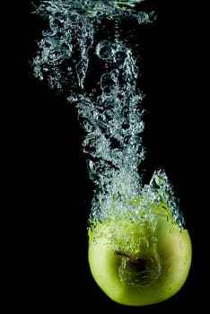 A green apple splashing on a water surface with a black background.