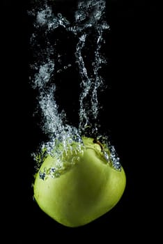 A green apple splashing on a water surface with a black background.