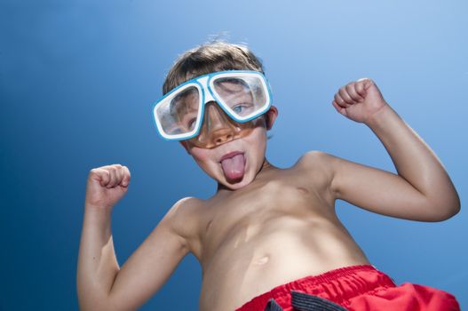 Young boy with attitude showing his muscles and wearig swiming googles