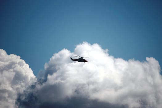A helicopter flying in front of a fluffy cloud