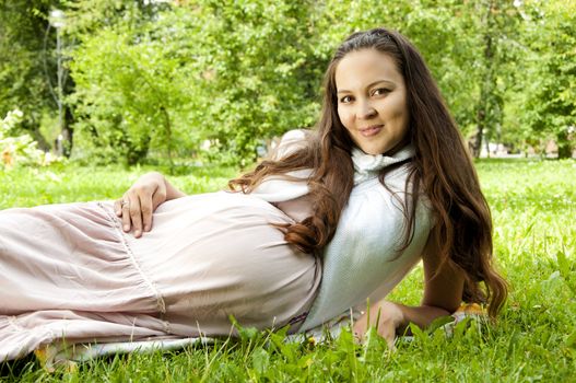 woman huging pregnant stomach, green grass background