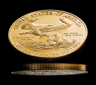 Close up of a solid gold eagle one ounce coin reflected in black shiny surface