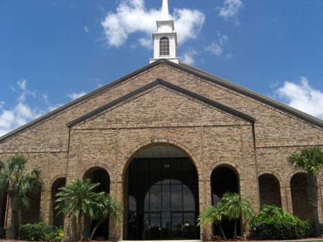 A church building with a high steeple on the roof, and against the blue skies.