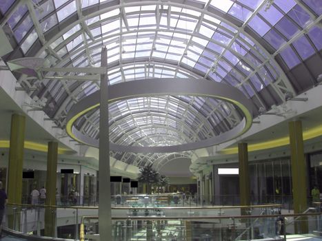 An extravagant interior of a shopping mall with steel beams, a skylight, staircases and designer shops.