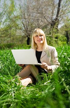 young businesswoman with laptop in green grass