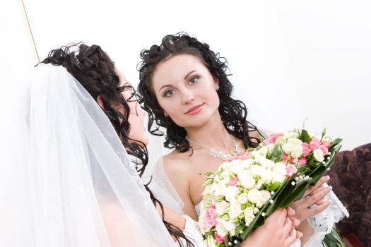 a beautiful bride with the bunch of flowers looking into the mirror