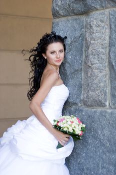 a beautiful bride by the stone wall with a bunch of flowers