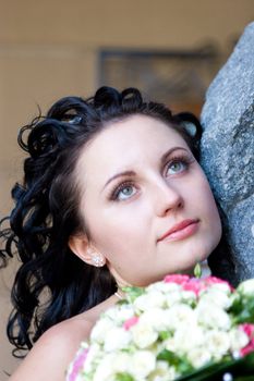 a girl by the stone wall looking up with the bouquet of flowers