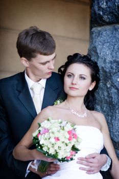 a portrait of the groom and the bride with a flower bouquet by the stone wall