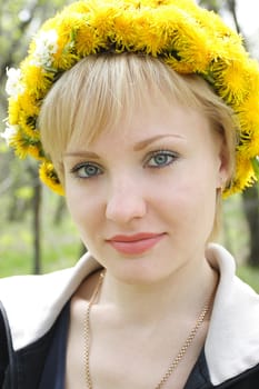 The young girl with a wreath from dandelions on a head