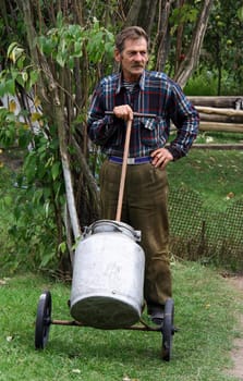 Man in checkered shirt standing and holding a cart with containers for water