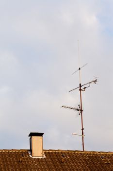 Old-fashioned analogue tv antenna on ceramic shingle rooftop.