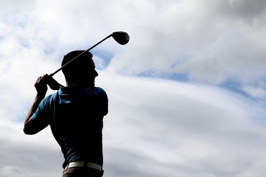 Young golfer driving with a wood against cloudy skies