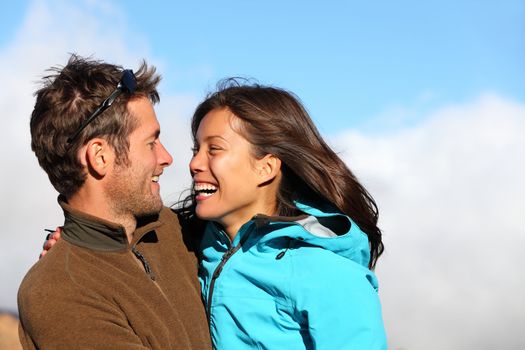 Happy young couple smiling outdoors looking at each other with love. Active young couple portrait during hiking holidays. Asian female model and Caucasian man model.