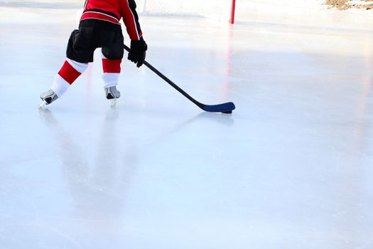 Young child playing ice hockey on a pond