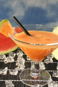 a glass of melon smoothie with cantaloupe melon pieces and ice cubes