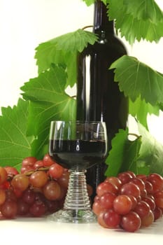 a glass of red wine with bottle, grapes and leaves