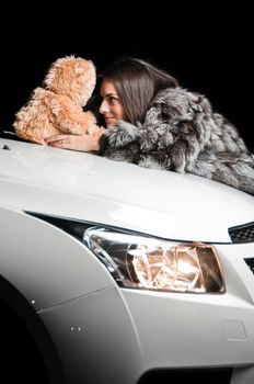Girl laying on white car hood with plush teddy bear