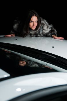Pretty girl in fur coat laying on car hood