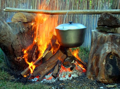 The kettle on a wooden crossbeam hangs over a fire
