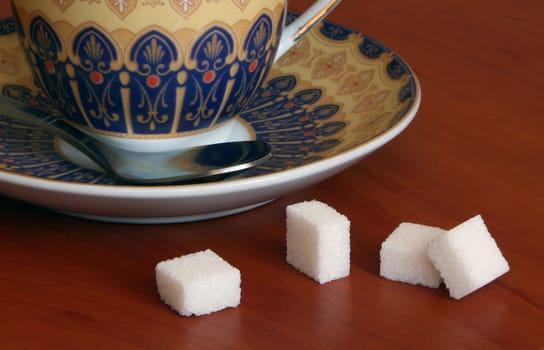 Pieces of sugar near a saucer. It is focused on sugar