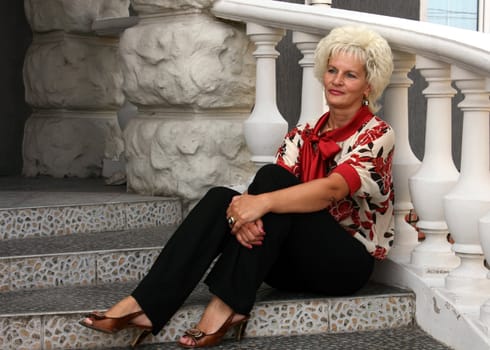 Woman in bright blouse and dark trousers sitting on the stairs