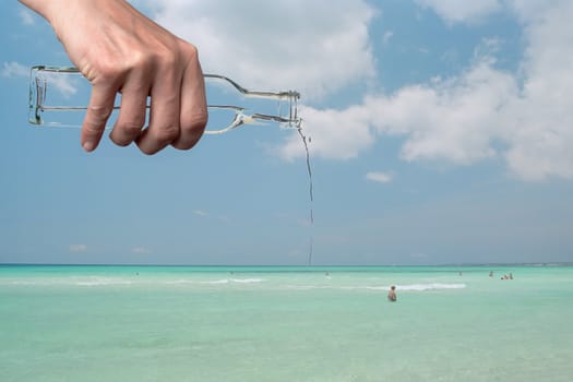 A hand holding a bottle pouring into the sea.