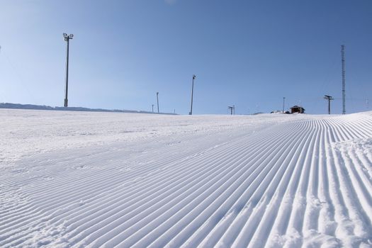 A newly groomed skislope under a clear blue sky