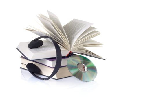 Books hadphones and a CD on a white background with a faint reflection suggesting the concept of audio books