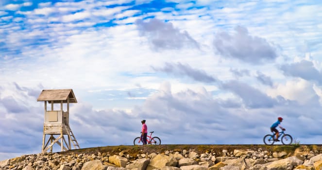 Men are towed bicycle and lighthouse at sunset.