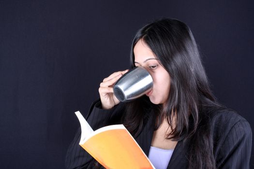 A beautiful Indian woman reading a book while drinking coffee.