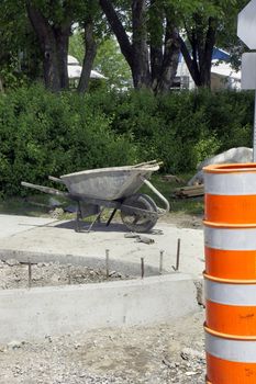 Wheelbarrow used for mixing concrete to be pourred in the new street corner sidewalk left with dirty gloves during lunch break, with cone warning of the construction zone.