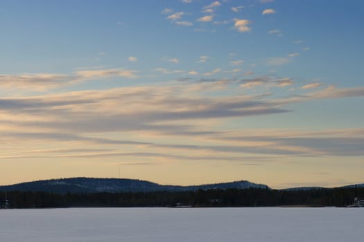 A frozen lake at sunset under a blue sky with some streaks of clouds