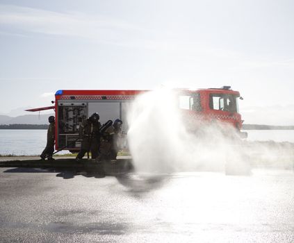 Fire fighters training, putting out a small fire next to the truck on a beautiful summer day