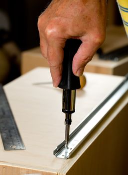 Screwing a screw into a drawer runner on side of wooden drawer