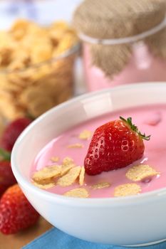 Strawberry yogurt with fresh strawberry and corn flakes with strawberries, corn flakes and yogurt in glass in the back (Selective Focus, Focus on the strawberry in the yogurt)